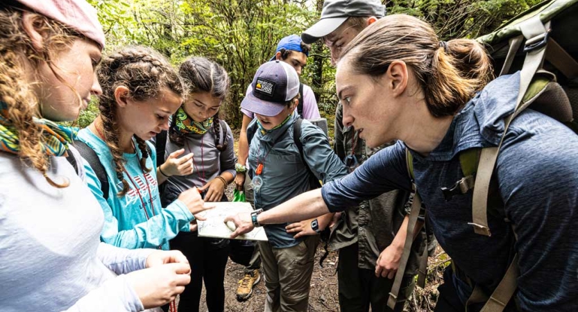 A group of young people examine a map in a wooded area. 